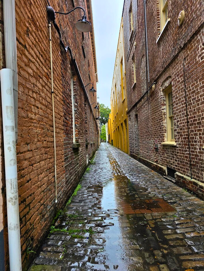 Keystone Justice. Amen by John Al, a narrow brick alley with wet pavement and strong perspective lines leading toward a brighter opening. 