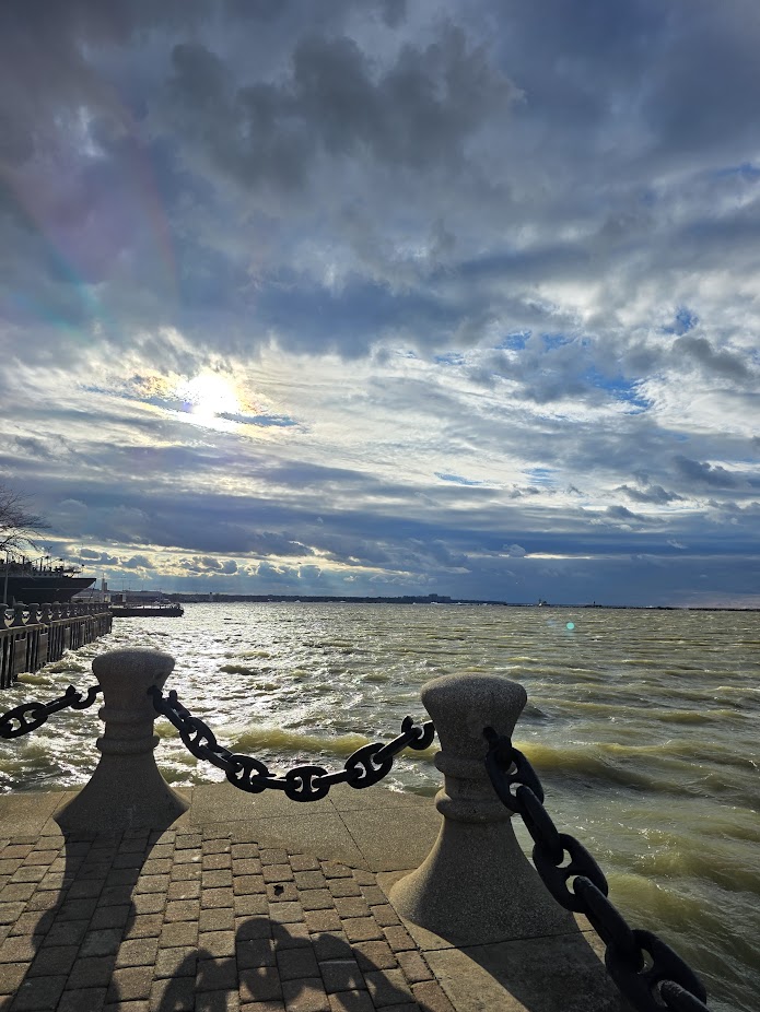 Moody waterfront with chained stone bollards, choppy water, and dramatic clouds.